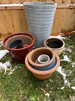 Overview of assorted planters showing terra cotta, dark brown, and black plastic pots arranged on grass with traces of snow.