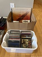 Box of vinyl records with Led Zeppelin record visible on top and plastic bin of assorted CDs below
