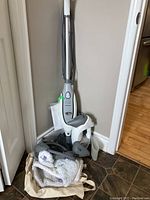 Full view of Shark upright steam cleaner, handheld steamer, and cleaning attachments on floor by wall corner.