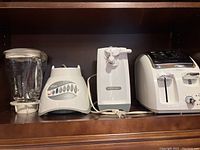 Oster blender, Proctor Silex can opener, and Avante Deluxe toaster shown side by side on shelf.