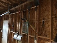 Garage wall with hanging garden and snow tools including shovels, rakes, broom, and pitchfork heads without handles