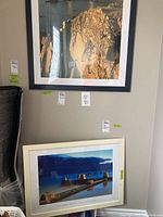 View of two framed water scenery photographs leaning against a wall, one with black frame and one with white frame