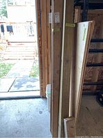 Photo showing several stacked wood planks of varying widths leaning against wall near a door.