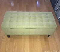 Full view of green upholstered bench with tufted cushion top and dark wooden legs, showing general wear.