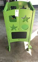 Front view of the green child's kitchen stand helper with star-shaped and other cutouts, including a chalkboard feature.