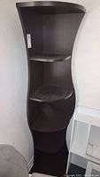 Full view of hourglass-shaped brown corner shelf unit showing all shelves and curved design.