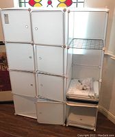 Overall view of the white cubical storage unit located in a room corner, showing multiple compartments with white doors and wire shelves on some units.