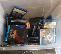 A plastic container with multiple Blu-ray and DVD discs visible including The Godfather and T2 Judgment Day.