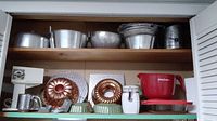 Shelf view showing various metal and copper finish baking pans and molds, a Betty Crocker mixing bowl, and a metal canister