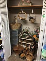Closet containing various wicker baskets stacked and hanging, plastic storage tower with drawers, assorted faux flowers in baskets.