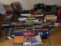 Wide overall view of the assortment of books arranged horizontally and vertically on a hardwood floor, visible variety of colors, sizes, and thicknesses