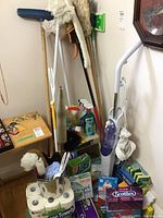 Photo showing mop, broom, dust mop, spray bottles, and assorted cleaning items on the floor and leaning against a wall.