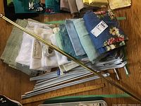 Curtains and rods assortment with fabric panels in different colors and floral patterns, brass curtain rod diagonally placed on top.