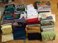 Wide view of assorted folded fabrics showing varied colors and patterns including florals, solids, and checks.