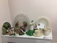 Overview of lot showing Belleek creamer and sugar bowl, Goebel Hummel figurines, decorative glass and porcelain platters, and various small decorative items.