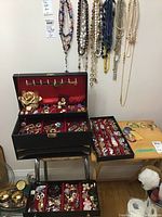 Wall display of hung necklaces and open jewelry box showing various earrings, brooches, pins, and a large metal rose