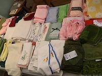 Photo of assorted linens spread on a surface, showing towels, washcloths, and embroidered pieces in various colors and fabrics.