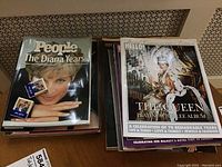 Two stacks of magazines including People and Hello magazines featuring Princess Diana and Queen Elizabeth II on covers