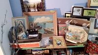 Photo showing framed painting with boat scene, GE tape recorder 3-5015, Minolta Freedom III camera, GE Super Cube batteries, various photo albums, prints and frames on a shelf.