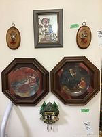 Overall lot showing all six items mounted on wall: two decorative plates, one small cuckoo clock wall decor, one framed picture, and two oval wall plaques