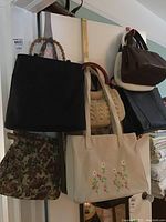 Handbags and purses hanging on a door including black handbag with bamboo handles, cream embroidered tote, floral tapestry bag.