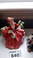 Front view of the Royal Doulton Lydia figurine showing the woman in red dress seated with green foliage.