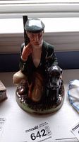 Front view of Royal Doulton figurine The Gamekeeper showing man kneeling with dog and shotgun.
