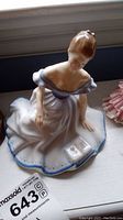 Porcelain figurine of woman reading seated, view from front showing dress and book.