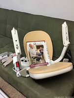 Disassembled beige padded stairlift seat with armrests, with acorn manual card on a couch.