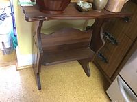 Side table with medium brown wood finish, curved edges, and decorative side panels. Shelf under the top surface visible.