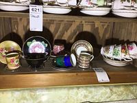 Shelf with various vintage teacups and saucers, different floral designs and colors.