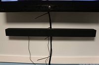 Black Vizio sound bar mounted below a TV with cables hanging down.