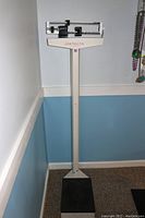 Full view of the Detecto physician beam scale showing the vertical stand and black weighing platform.