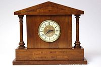 Front view of large wooden mantle clock showing triangular pediment top, circular clock face with Roman numerals, and turned wooden columns on each side.