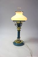 Side view of ornate electric lamp with illuminated white glass shade and brass and blue base.