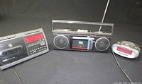 Photo showing all three items together: GE cassette clock radio, vintage boombox cassette radio, and small digital alarm clock.