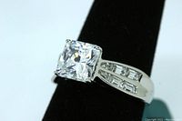 Close-up photo of the radiant cut solitaire simulant diamond engagement ring on a black ring holder showing the size and setting of the stones.
