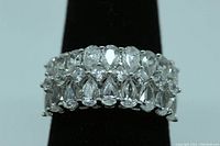 Close-up front view of a sterling silver ring displaying rows of clear emerald cut and pear cut simulated diamond stones on a black ring display.