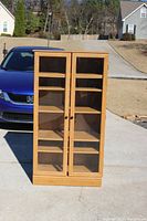 Front view of the tall oak display cabinet with glass doors closed, showing its natural wood finish and clean design.