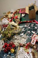 Wide view showing various Christmas decorations including boxes of glass ornaments, pewter ornaments, crocheted stars, thread spool wreaths, elves, and playing cards laid on a table.