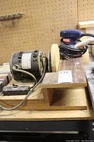 Side view of the electric bench grinder mounted on a wooden base showing the circular grinding wheel and motor with GE label.