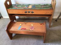 Two handcrafted wooden benches, larger with heart cutouts on sides and painted top, smaller with curved seat and painted scene of children and apples