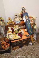 Photo showing overall lot contents including stuffed scarecrows, metal sign, boxed lighted pumpkin, decorative pumpkins, and more.