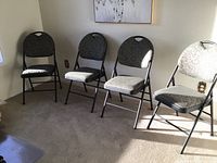 Four cushioned folding chairs arranged spaced apart on carpeted floor with sunlight from window.