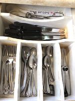 Drawer with stainless steel forks, soup spoons, teaspoons, table knives, steak knives, and kitchen scissors.