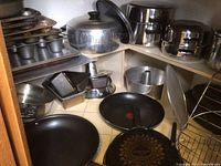 Full assortment of metal bakeware including stock pots, loaf pans, springform pans, cookie sheets and baking molds arranged on shelves and floor.