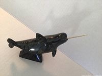 Side angle view showing the dark stone narwhal carving with horn and base.