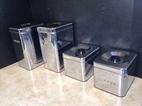 Set of four vintage metal canisters arranged in a row showing the front labels Sugar, Flour, Tea, and Coffee.