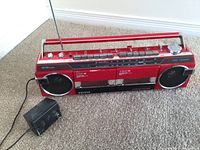 Front side view of the red SANYO boombox with power adapter on carpet.