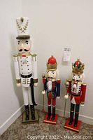 Frontal view of three wooden nutcrackers of varying heights and colors against a white wall.